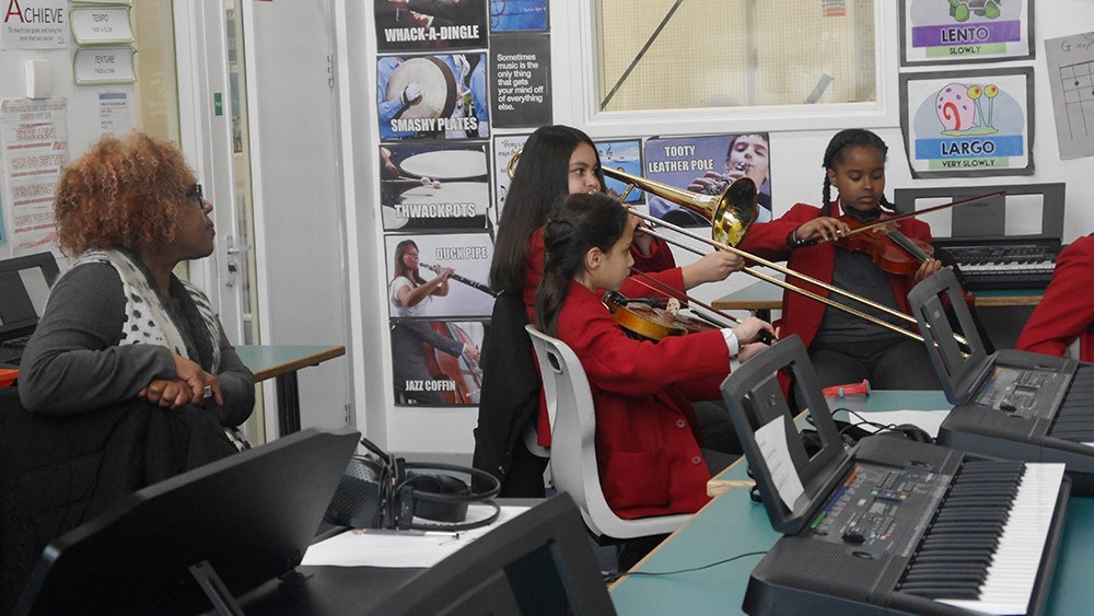 Three Swanlea students in red uniforms play violins and trombone, while Errollyn listens