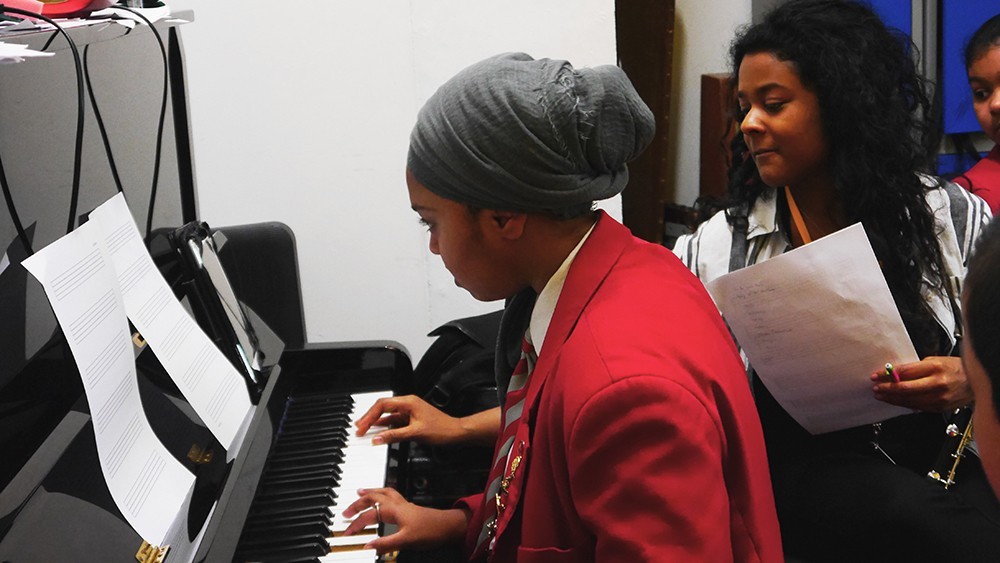 A Swanlea school student in a red uniform and Ishani O'Connor from Chineke Orchestra play the piano together