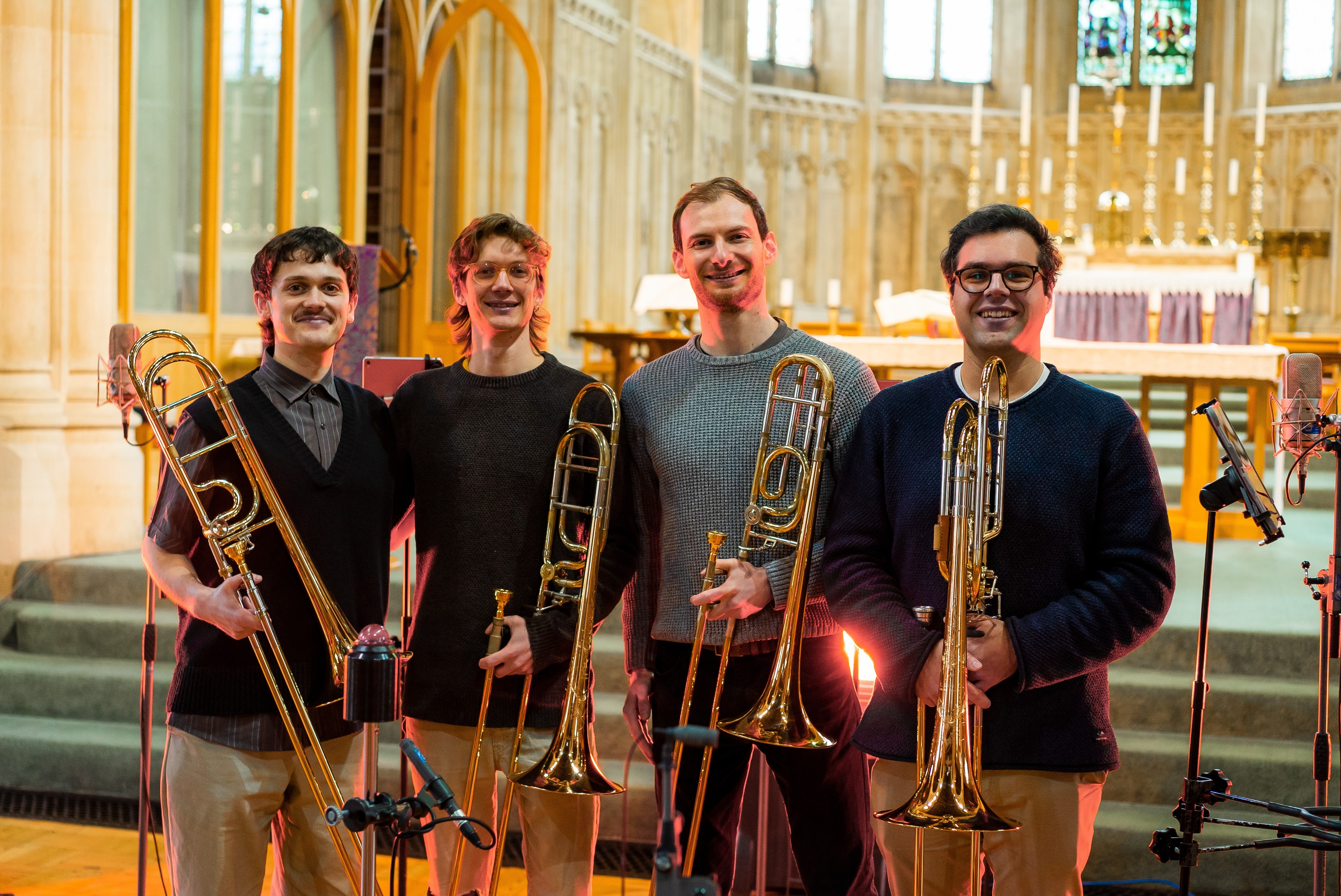 Slide Action in a church. A group of four men holding trombones and similing.