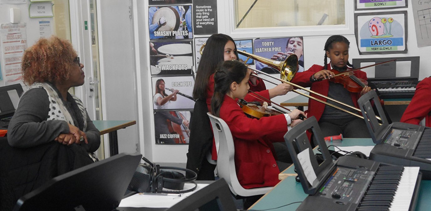 Three Swanlea students in red uniforms play violins and trombone, while Errollyn listens