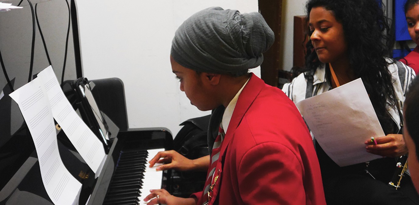 A Swanlea school student in a red uniform and Ishani O'Connor from Chineke Orchestra play the piano together